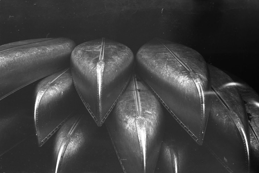 A black and white photo of a stack of aluminum canoes.