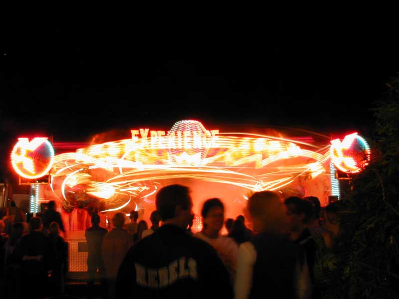 A color, long-exposure photo of a carnival ride showing light trails. The ride is called EXperience.