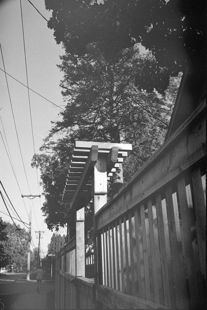 A black and white photo of a wooden fence gate, taken from along side the fence.