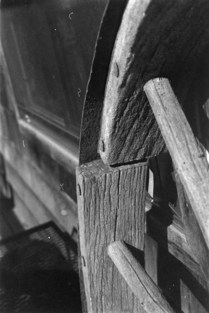 A black and white photo of the edge of a wooden wheel. Age and weather have misaligned the wheel.