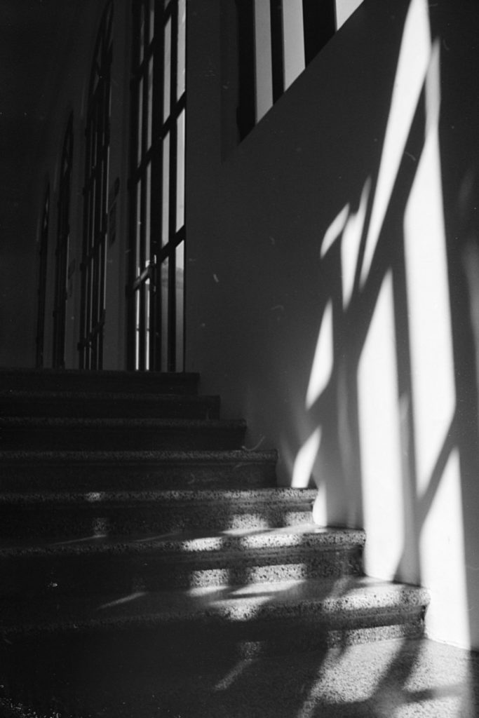 A staircase partially lit by light from behind. Shadows of the window pane structure cross the steps.