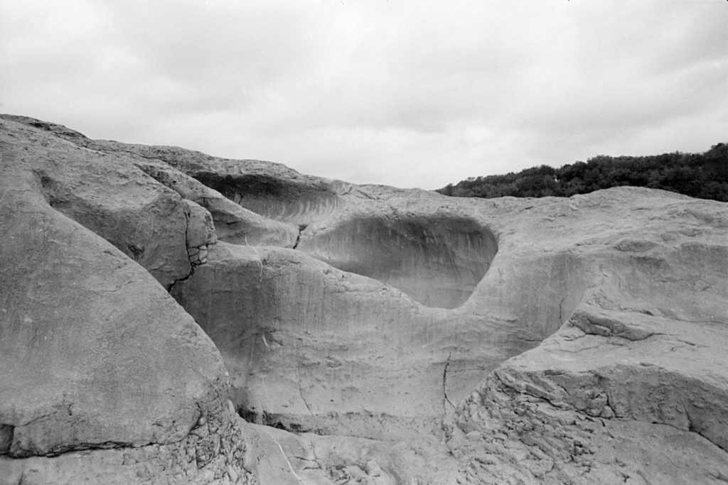 A black and white photo of a large, water worn rock full of indentations and channels.