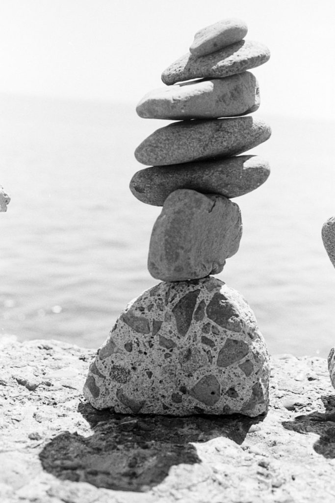 A black and white photos of a tall cairn of stones sitting on a rock, with Lake Superior in the background